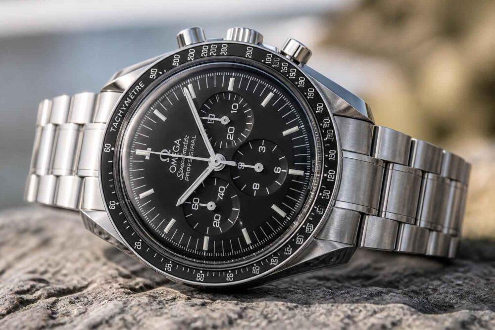 Srebrny zegarek Omega Speedmaster z czarną tarczą leży na skale